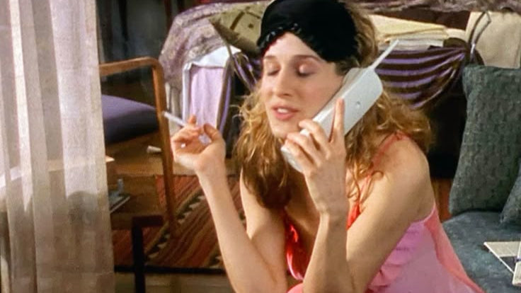 Woman in a pink nightgown talking on a phone in a cluttered room.